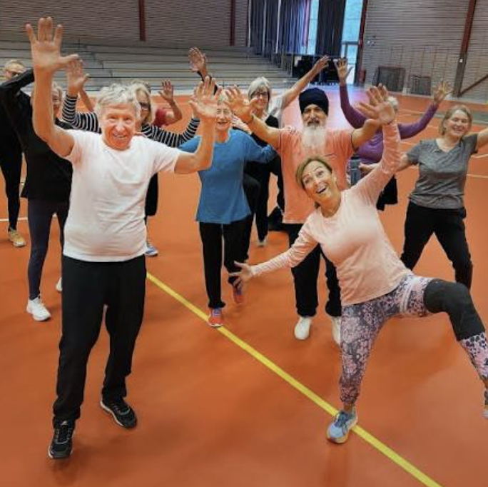 A group of older adults smiling and raising their arms during a group exercise session